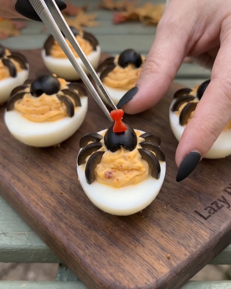 Placing an olive spider with a red hourglass on a deviled egg