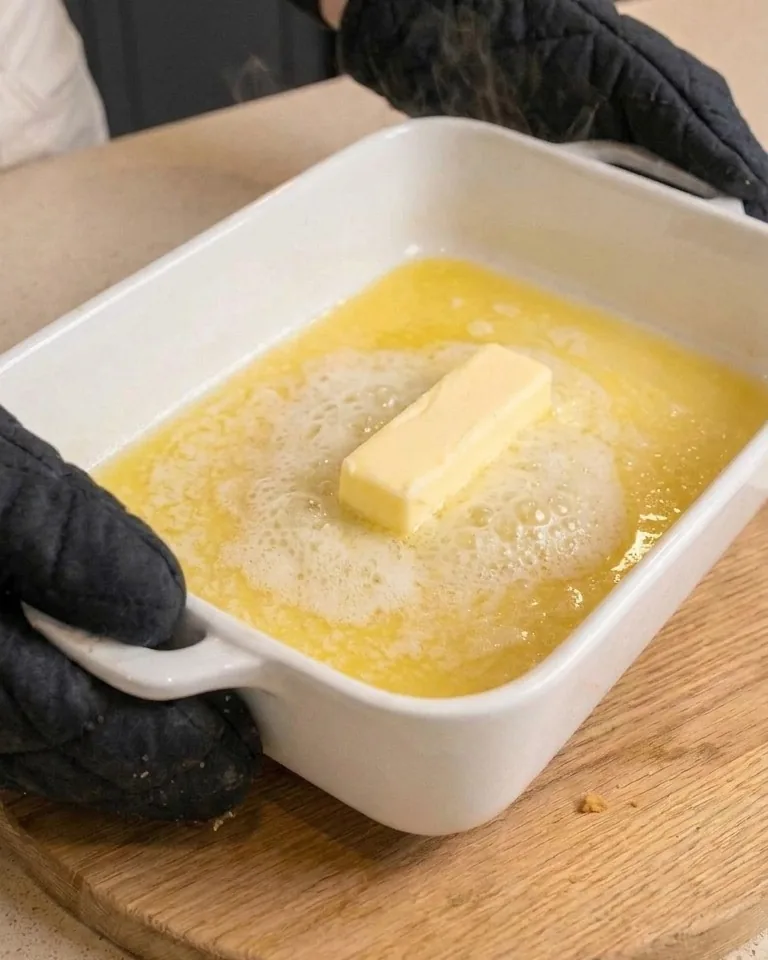 A stick of butter melting in a white baking dish